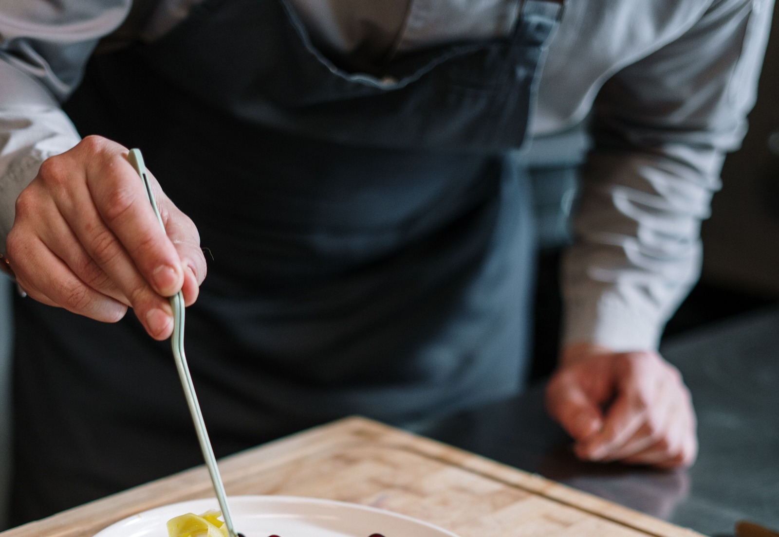 Chef's hands using precision tweezers to finish a colourful dish on white porcelain